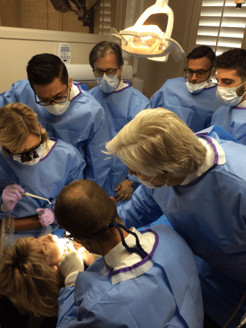 A group of dentists watch as Dr. Kosinski demonstrates a dental procedure on a patient
